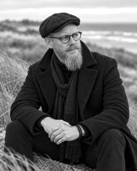 Mirko Schwerdtfeger in Mantel und Schiebermütze, sitzend in den Dünen von Spiekeroog